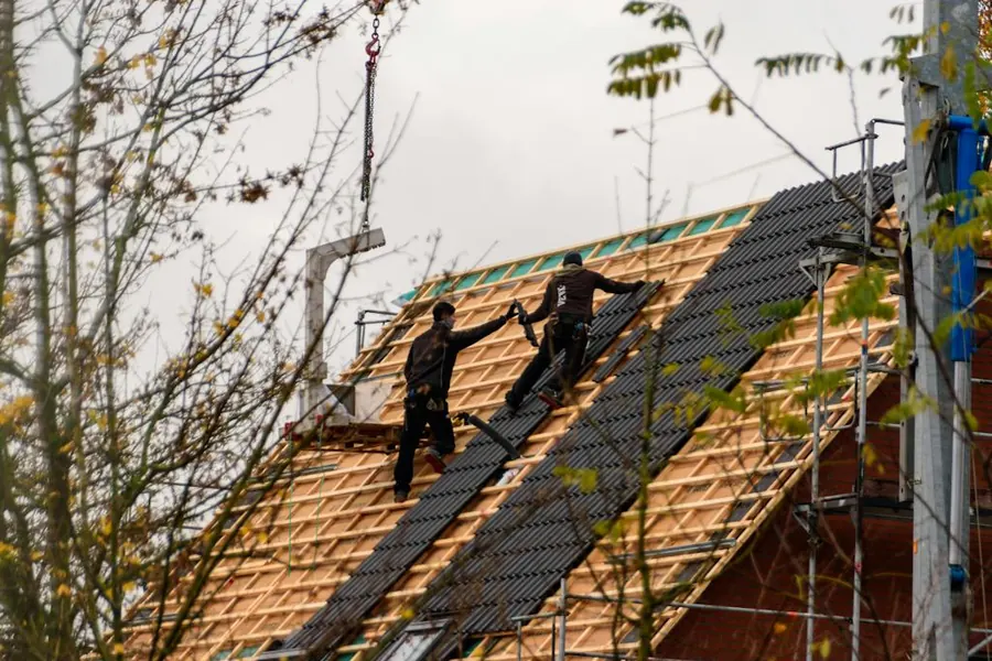 Two roofers setting dark tiles on an open roof frame